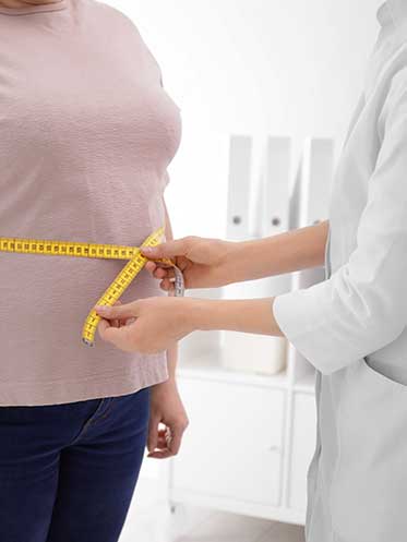 Doctor measuring a patient's waist with a tape measure, representing reduced inflammation and improved metabolism.
