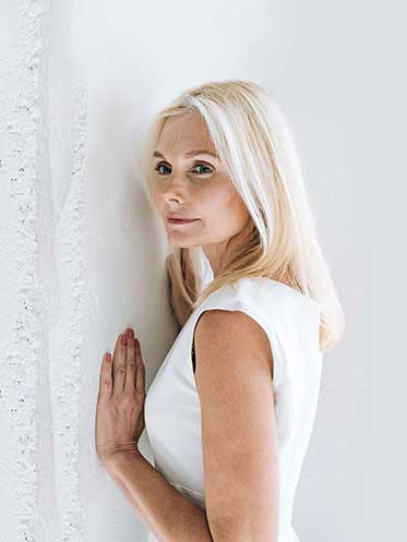 A confident midlife woman standing in natural light, smiling softly — symbolizing health, clarity, and the shift toward personalized hormone care.