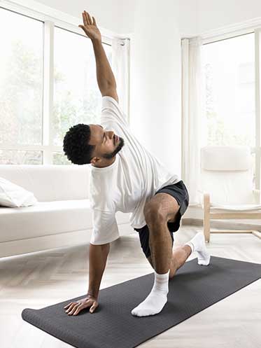 Middle-aged Black man stretching in his living room, practicing gentle movement to support flexibility, stress regulation, and overall metabolic health.